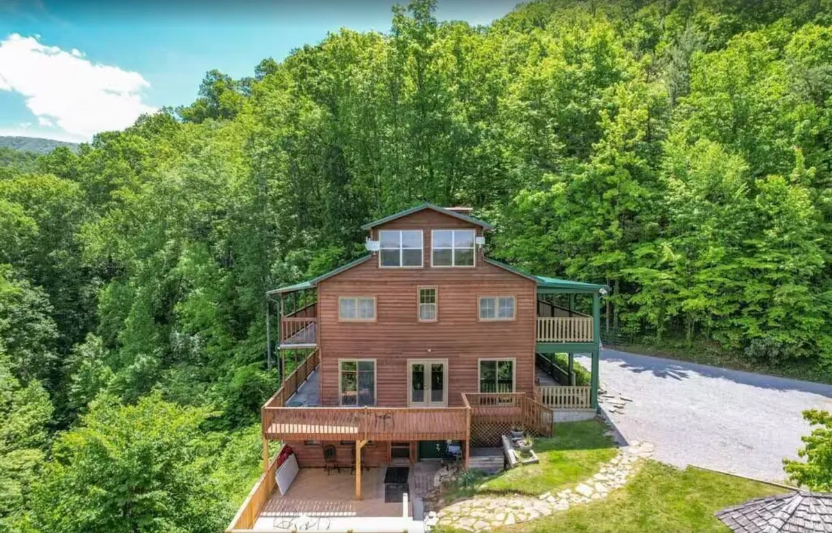 This image shows the wooden exterior of the lodge nestled among lush greenery, with balconies and a pathway leading up to the house. The scene captures the welcoming and spacious feel of the property, set against a peaceful natural backdrop.
