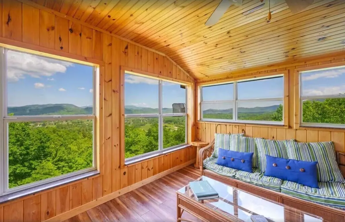 A peaceful reading lounge with large windows, wood-paneled walls, a cushioned couch, and a coffee table. The scene is bathed in natural light, providing a cozy spot to relax, read, or enjoy the surrounding views in solitude or with company.