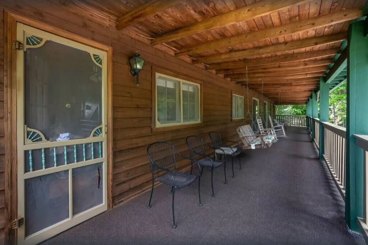 This image features the exterior porch area with rocking chairs, wooden beams, and a screen door, capturing a relaxing outdoor spot perfect for unwinding or socializing. The calm atmosphere hints at both family gatherings and quiet moments, reflecting the flexible use of the lodge's entertainment spaces.