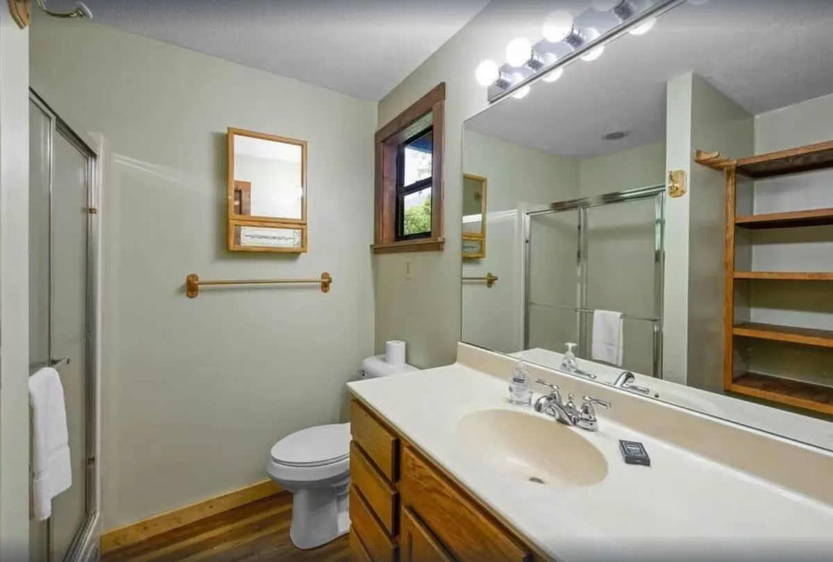 A well-appointed bathroom featuring a sink, mirrors, shower area, toilet, and wooden shelves. The atmosphere is serene, clean, and inviting, with thoughtful details that provide comfort and privacy.