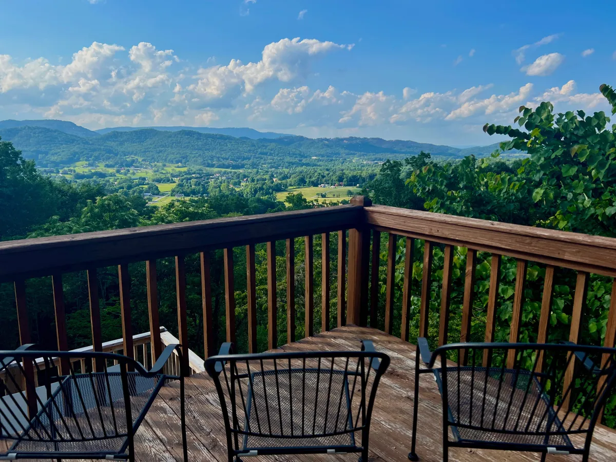 This image depicts a deck with comfortable chairs overlooking a breathtaking mountain view, surrounded by lush greenery. The tranquil setting invites relaxation and socializing in the fresh air, enhancing the sense of a resort getaway.