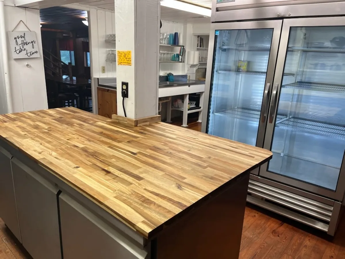 This image showcases a warm and inviting kitchen area with a wooden countertop, a visible refrigerator, and open shelves stocked with glassware. The space appears spacious and well-equipped, emphasizing both the rustic charm of the lodge and its practicality for group cooking and gatherings.