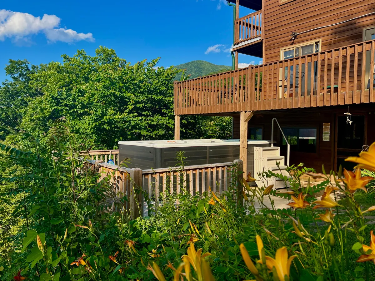 This image features a wooden deck with a hot tub, overlooking lush greenery and distant mountains. The deck area embodies both relaxation and a direct connection to the outdoors, offering scenic views ideal for unwinding after exploring nearby attractions.