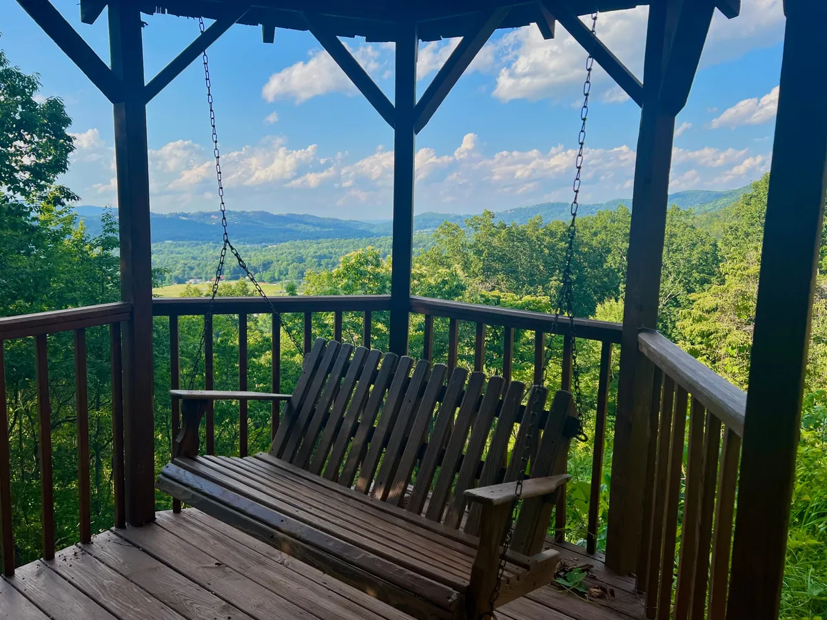 This image features a charming swinging bench set on a deck, perfectly positioned to take in the sweeping mountain views. Surrounded by lush greenery and trees, the tranquil setup invites guests to relax, read, or simply soak up the peaceful sounds of nature.